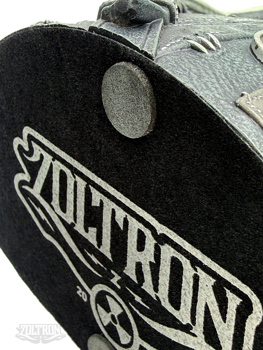 A close-up of a the bottom silkscreened, felt base of a highly detailed resin and soapstone sculpture by artist Zoltron, featuring a highly detailed skull figurine wearing a cracked leather aviator helmet, a weathered black leather jacket, war medallions and adornments, smoking a cigarette, set against a plain white background.